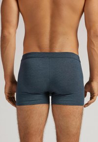 Tmavě modré boxerky s hladkým povrchem a měkkým pasem, které poskytují těsný střih a minimální švy. Zadní pohled zvýrazňuje design.