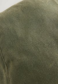 Olivgrüner Stoff mit einer strukturierten Oberfläche, der ein feines Webmuster und eine sichtbare Naht aufweist. Das Material wirkt weich und langlebig.