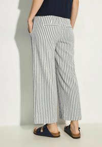 Wide-legged trousers with vertical navy and white stripes, featuring side pockets and a relaxed fit. Paired with dark sandals.