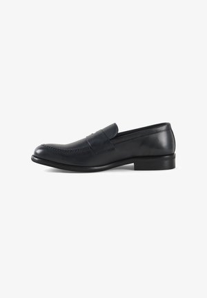 Mocasín de cuero negro con puntera redonda y detalles de costura. Presenta una correa frontal y una suela plana y lisa. Vista lateral mostrada.