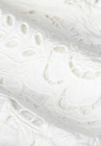 Weißer bestickter Stoff mit komplexen Schlaufen- und Ausschnittmustern. Weiche Textur mit sichtbaren Fadendetails und Schichtung.