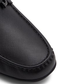 Zapato de cuero negro con superficie texturizada, detalles de costura y punta redondeada. Presenta una hebilla decorativa en el lado superior.