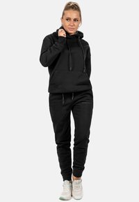 Set di felpa nera con cappuccio e pantaloni sportivi in morbido tessuto, con tasca a canguro, cordini e polsini a coste. Abbinato a sneakers bianche.