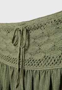 Tissu vert olive avec motifs de feuilles tricotées, détails en ajouré, un cordon à nouer, et une section de tissu froncé et froissé en dessous.