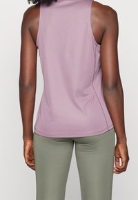 Lilla ærmeløs top med en glat tekstur og tætsiddende design, kombineret med olivengrønne leggings. Enkle syningsdetaljer er synlige.