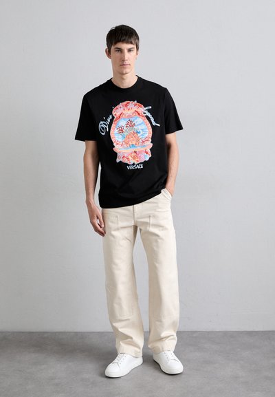 T-shirt en coton noir avec un imprimé graphique coloré d'un coquillage et de corail. Associé à un pantalon ample beige clair et des baskets blanches.