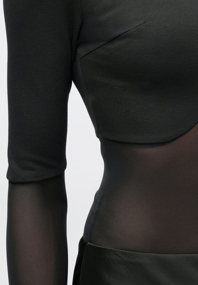 Top negru cu mâneci lungi transparente, având un corset solid texturat și o secțiune netedă, semi-transparentă la talie.