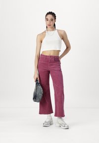 Felroze corduroy wijde broek, gecombineerd met een witte haltertop. De outfit bevat een gestructureerde stof en een zilveren ketting.