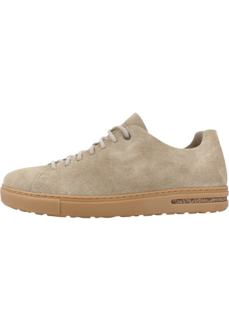 Beige suedey sneaker med rund tå, lyse snørebånd og en tan gummisåle. Har et teksturert sidedetail nær sålen.