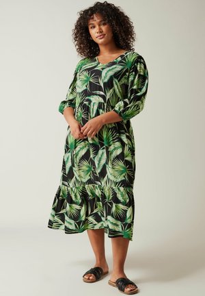 Losse midi-jurk van zwart materiaal met een levendig groen tropisch bladerenpatroon, driekwartmouwen en een gelaagde onderrand.