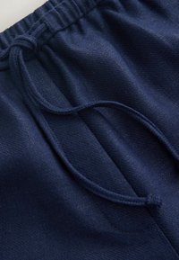 Detailný záber na tmavomodré tepláky s elastickým pásom a zauzleným šnúrkovým sťahovaním.