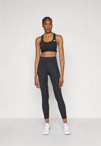 Sort sports-bh og leggings sæt lavet af strækbart stof. Bh'en har en rund halsudskæring; leggings er højtaljede med en glat tekstur.