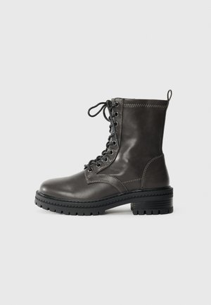 Mörkgrå läderankelboot med snörning fram, kraftig strukturerad sula och sydda detaljer längs övre kanten. Rund tådesign.