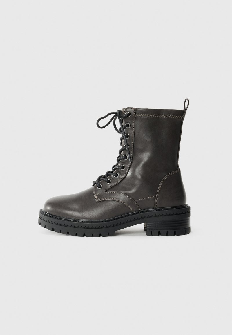 Bottines en cuir gris foncé avec avant lacé, semelle texturée robuste et détails cousus le long du bord supérieur. Design à bout rond.