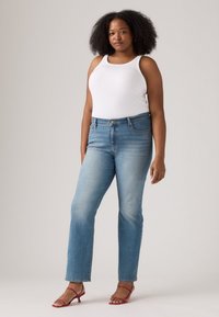 Lyseblå rettskårne jeans med en falmet finish. Kombinert med en hvit tanktop og røde sandaler med stropper, som fremhever et uformelt antrekk.