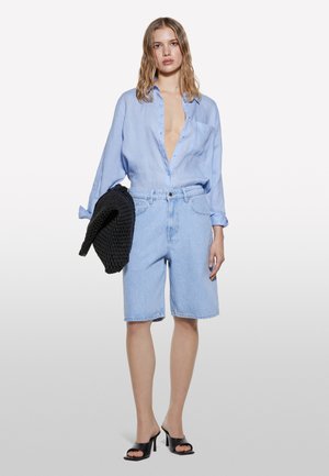 Light blue linen shirt with a deep V-neck, paired with light blue denim shorts. Black knitted bag and black open-toe heels complete the look.