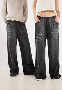 Lässige schwarze Jeans mit ausgewaschenen Wischdetails, elastischem Bund, Seitentaschen und einer strukturierten Oberfläche. Tragen mit lässigen Schuhen.