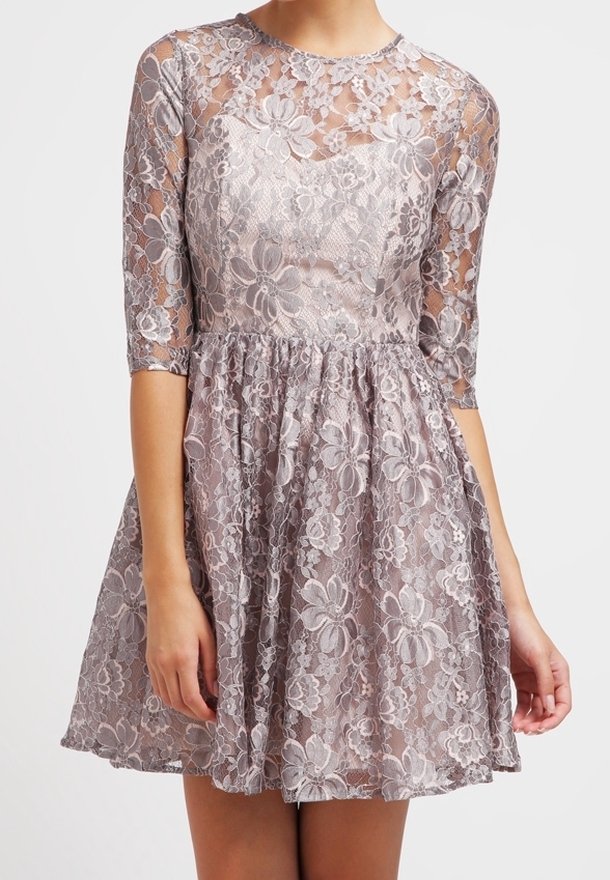 Robe en dentelle avec un corsage ajusté et une jupe évasée, présentant des motifs floraux et des manches trois-quarts de couleur lavande claire. Détail de superposition texturée.