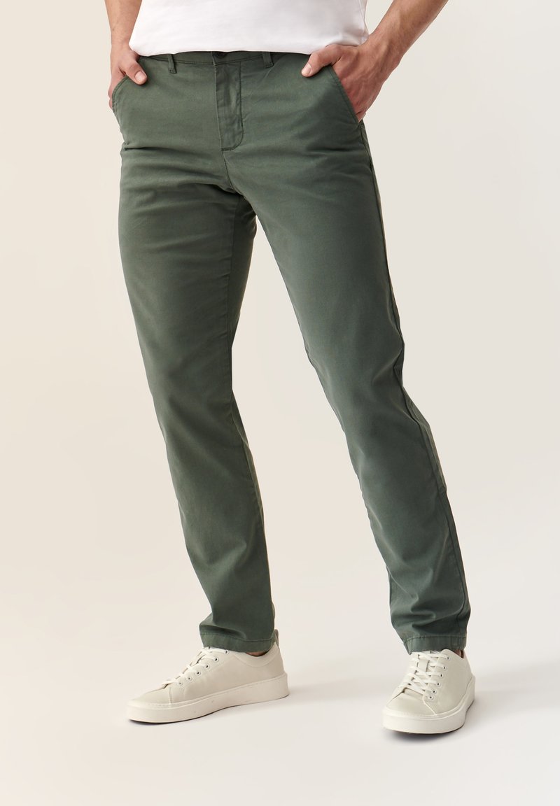 Chinos verdes de algodón con un corte ajustado, que cuentan con bolsillos laterales y una textura suave, combinados con zapatillas blancas.