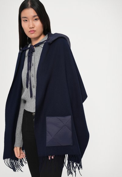 Poncho navy cu glugă, cu margine franjurată și detaliu de buzunar matlasat; realizat dintr-un material moale și texturat.