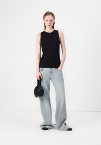 Svart ribbet ermeløs topp kombinert med lyseblå vide jeans. Modellen holder en liten svart veske, som viser en enkel, moderne silhuett.