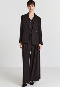 Completo nero su misura con giacca doppiopetto e pantaloni a gamba larga, caratterizzato da un tessuto testurizzato e bottoni decorativi sul gilet.