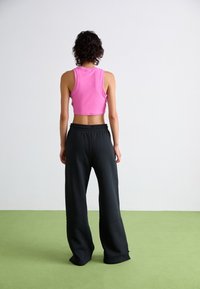 Rosa, kurz geschnittenes Tanktop und lockere schwarze Sweatpants. Das Tanktop hat einen runden Halsausschnitt, und die Sweatpants verfügen über einen elastischen Bund und weit geschnittene Beine.