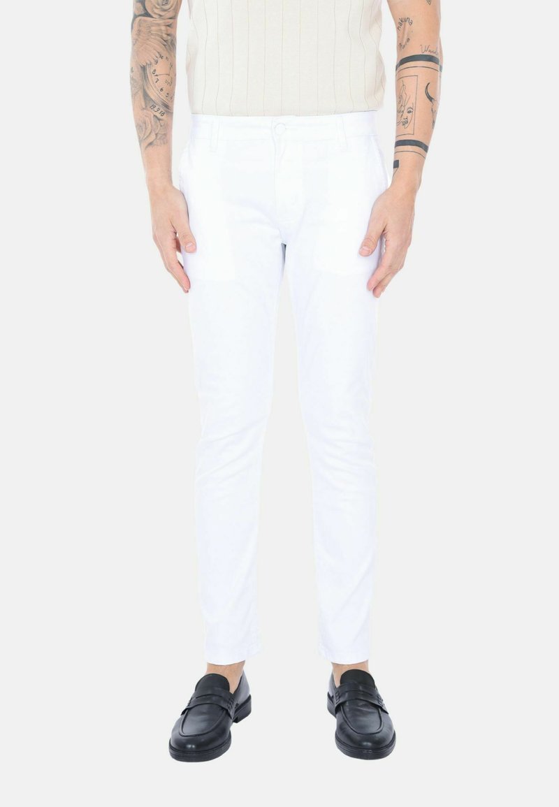 Pantaloni bianchi slim-fit in cotone, con una texture liscia, zip frontale e tasche laterali, abbinati a mocassini neri.