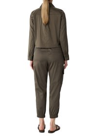 Olijfgroene cropped jas met knoopmanchetten, gecombineerd met bijpassende tapered cargobroek met elastische manchetten en zijzakken. Platte sandalen.