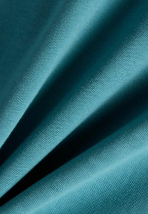 Zacht, stof in een teal kleur met een zichtbare fijne breistructuur en zachte plooien die schaduwen en diepte creëren.