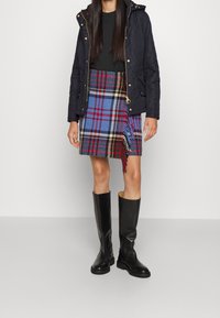 Granatowa pikowana kurtka, zielona koszula, spódnica w kratę w kolorach niebieskim, czerwonym i żółtym oraz czarne kozaki za kolano o teksturowanej powierzchni.