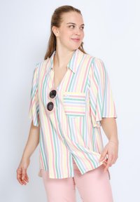 Chemise à manches courtes rayée dans des couleurs pastel avec une poche, ornée de boutons et d'un petit motif floral. Accentuée par des lunettes de soleil rondes.