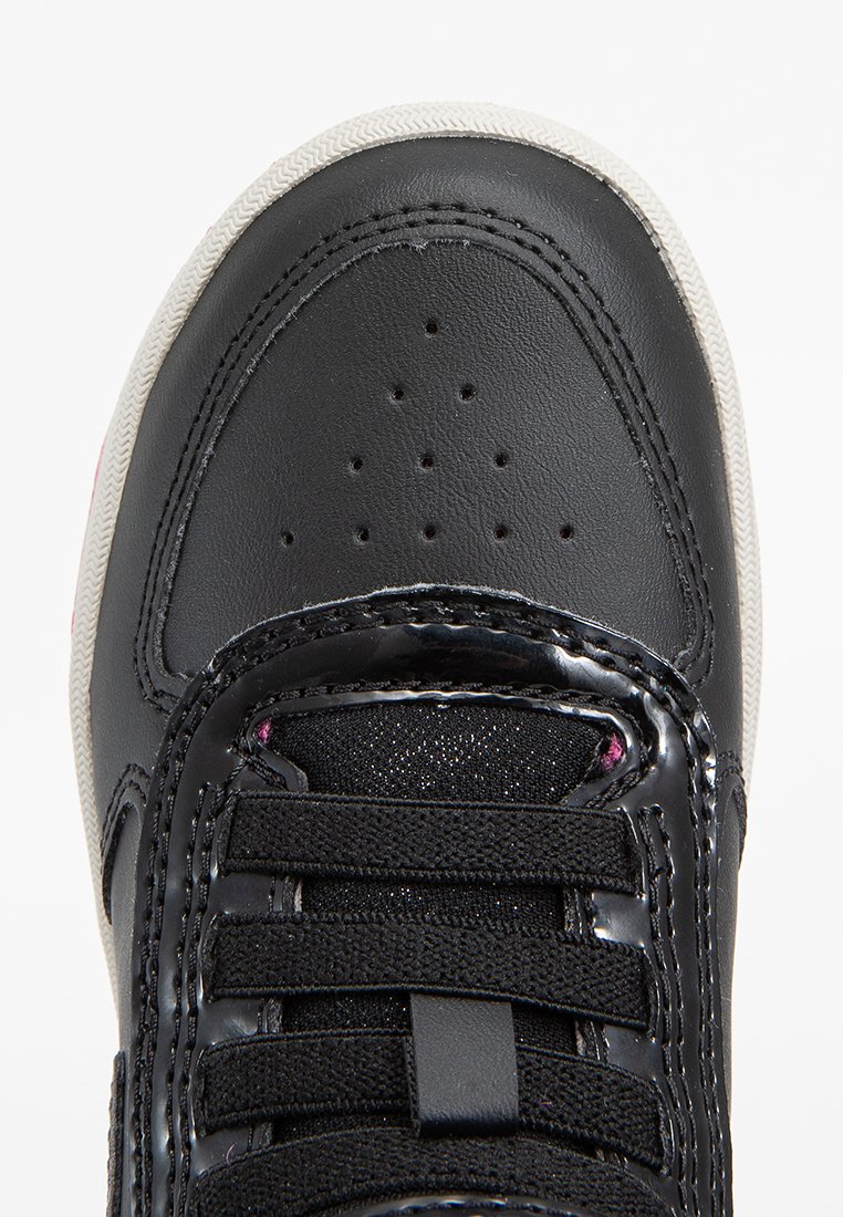 Zapato negro con parte superior de cuero liso, cordones negros texturizados y suela de goma blanca. Presenta pequeños agujeros de ventilación en la punta.