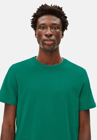 Grünes Baumwoll-T-Shirt mit Rundhalsausschnitt, kurzen Ärmeln und glatter Textur, mit einem lässigen Schnitt und ohne sichtbare Muster oder Grafiken.