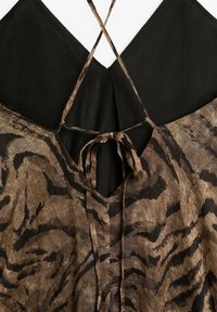 Robe en lin à motifs marron et noir avec un dos en V profond, nouée au cou et présentant un design léger et texturé.