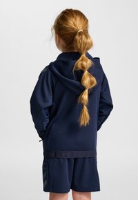 Mörkblå hoodie med huva, långa ärmar och elastiska muddar, kombinerad med matchande shorts med en logotyp och geometriskt mönster på sidan.