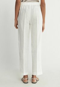 Weiße Leinenhose mit elastischem Bund, geraden Beinen und Seitennähten. Kombiniert mit hellen Sandalen.