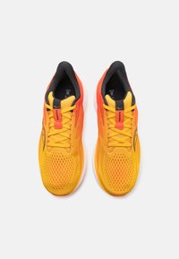 Des chaussures de course jaunes et orange dotées d'une tige en mesh, de lacets ronds, d'une semelle rembourrée et d'accents noirs le long du col et du logo.