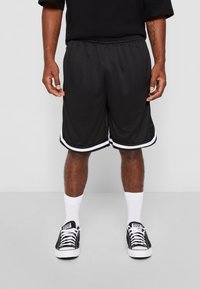 Shorts de sport noirs avec des bandes latérales blanches, ceinture élastique et tissu respirant, portés avec des chaussettes blanches et des baskets noires.