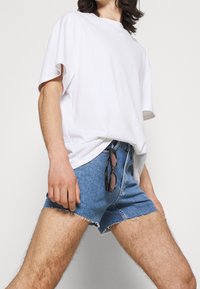 Vit bomullsoverstor t-shirt i kombination med blå denimshorts med en fransad fåll. Solglasögon hänger från shortsens bältesöglor.