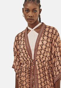 Prenda de estilo kimono con estampado que presenta una base marrón con motivos florales en tonos durazno y crema, bordes detallados y una cintura entallada.