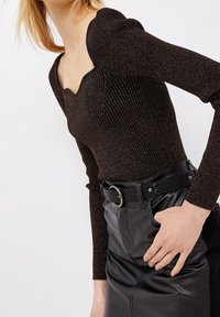 Dunkelbraunes geripptes Strickoberteil mit einem quadratischen Ausschnitt und puffärmel, kombiniert mit einem schwarzen Lederrock und einem Gürtel mit einer runden Schnalle.