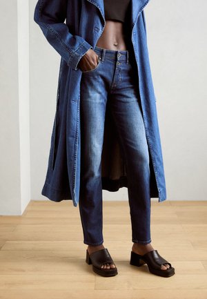 Denim overcoat with wide lapels, high-waisted blue jeans, and black open-toe block-heeled sandals. Smooth textures and light wash denim.