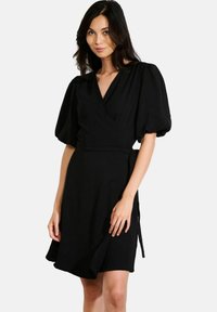 Robe noire drapée avec des manches courtes bouffantes, un décolleté en V, et une ceinture à la taille. Tissu lisse avec un ourlet fluide.