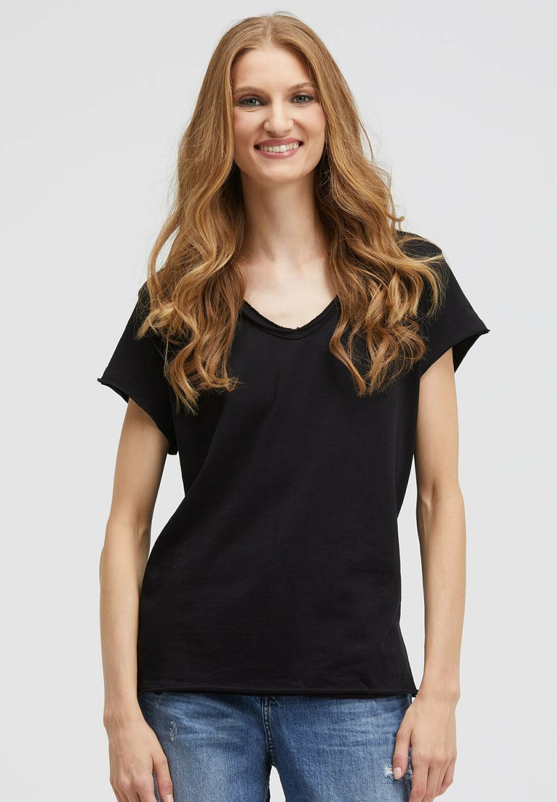 Schwarzes T-Shirt mit kurzen Ärmeln und entspanntem V-Ausschnitt, aus weichem Stoff gefertigt, mit lockerer Passform und glatter Textur, kombiniert mit blauen Jeans.