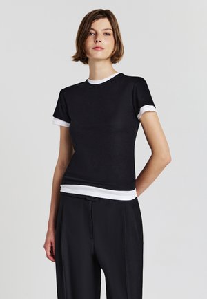 Maglietta nera a maniche corte con bordo e orlo bianco, design aderente, presentata su uno sfondo neutro.