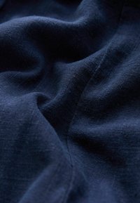 Tessuto blu scuro con una texture morbida e liscia e trama visibile, che mostra pieghe e increspature delicate.