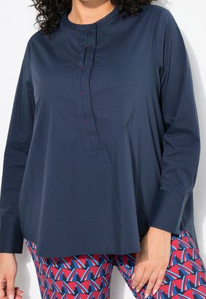 Person wearing a loose, long-sleeve navy blue shirt with a partial button placket and patterned red, blue, and white geometric pants.