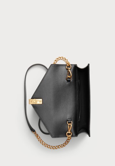 Sac à main en cuir noir avec bandoulière chaîne dorée, rabat ouvert montrant le compartiment intérieur et fermeture à boucle dorée sur fond clair.
