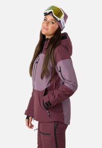 Giacca da sci bordeaux e lavanda con cappuccio, dotata di tasche con zip, design elegante e dettagli neri su polsini e zip.